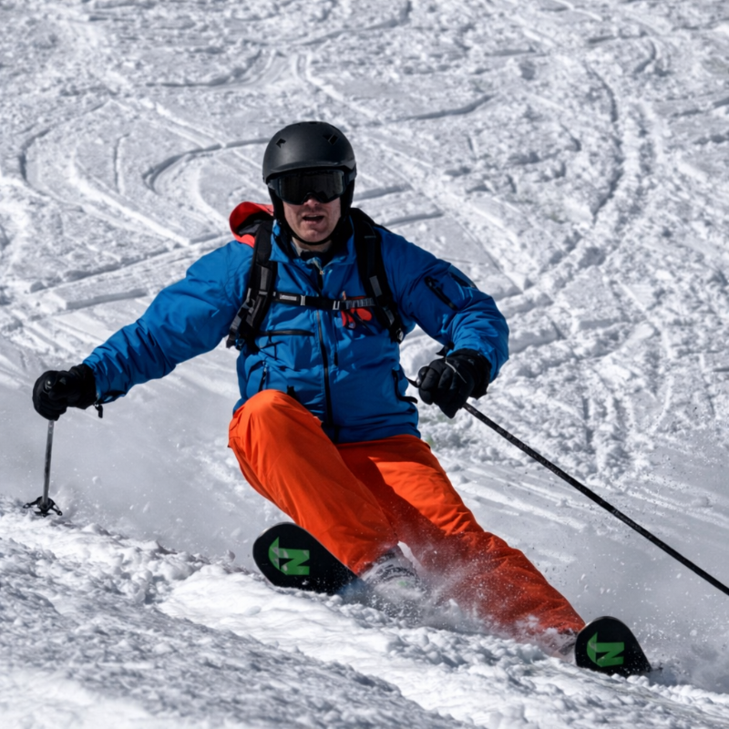 Skier in blue jacket and orange pants skiing down a snowy slope